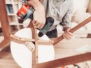 Furniture Assembler with Drill in Hands Repairs Chair.
