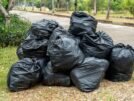 Black garbage bags on the road with green grass and plants background