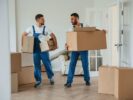 Boxes in hands. Two moving service employees in a room